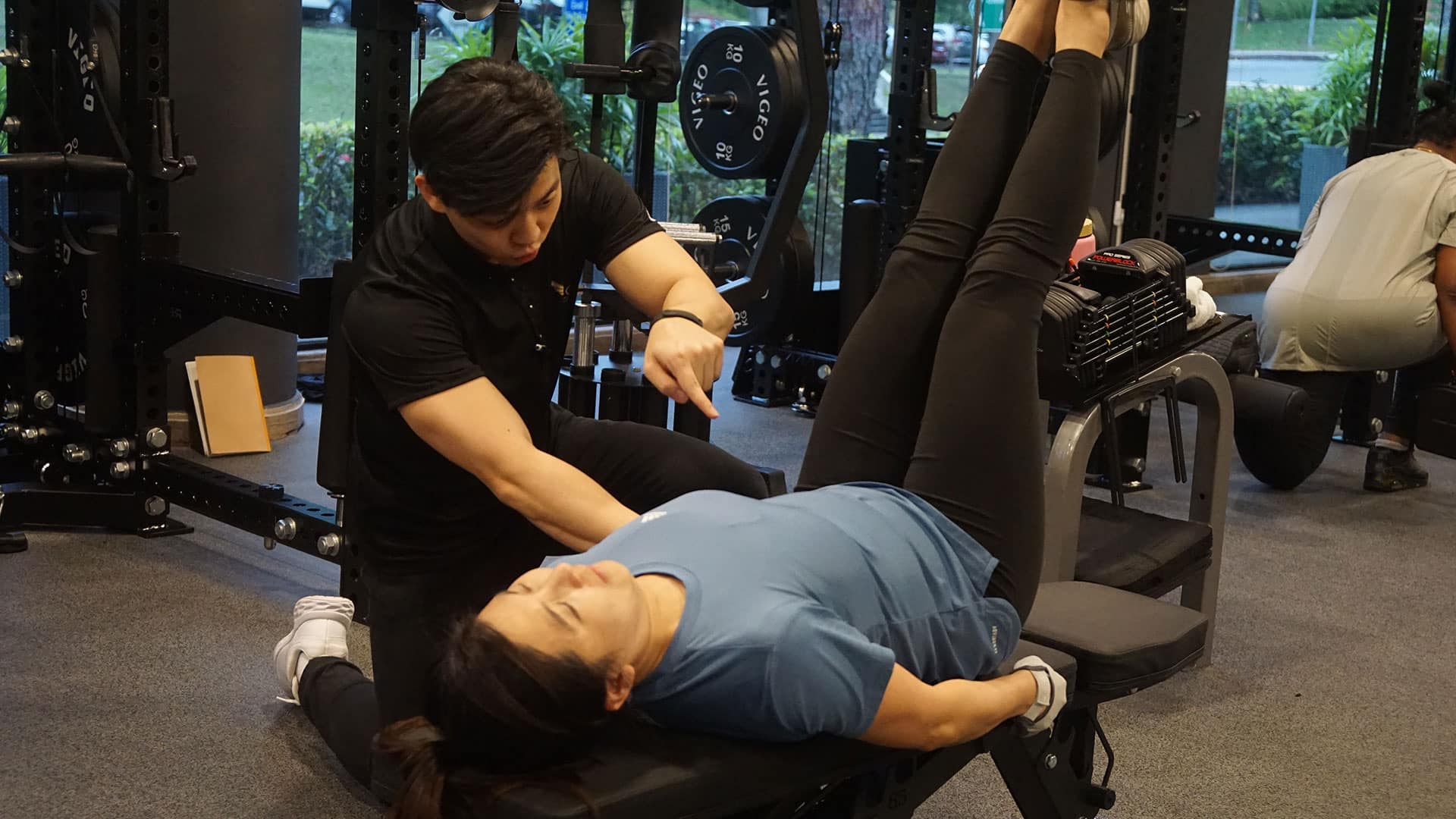 Professional fitness coach assisting with weight training in gym.