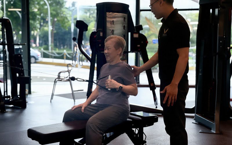 Senior woman doing seated cable row exercise with personal trainer