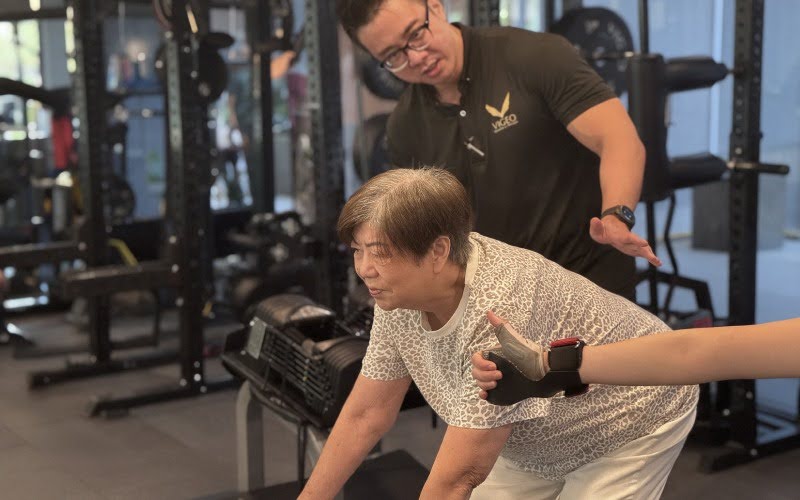 Senior woman performing dumbbell rows to prevent sarcopenia with trainer