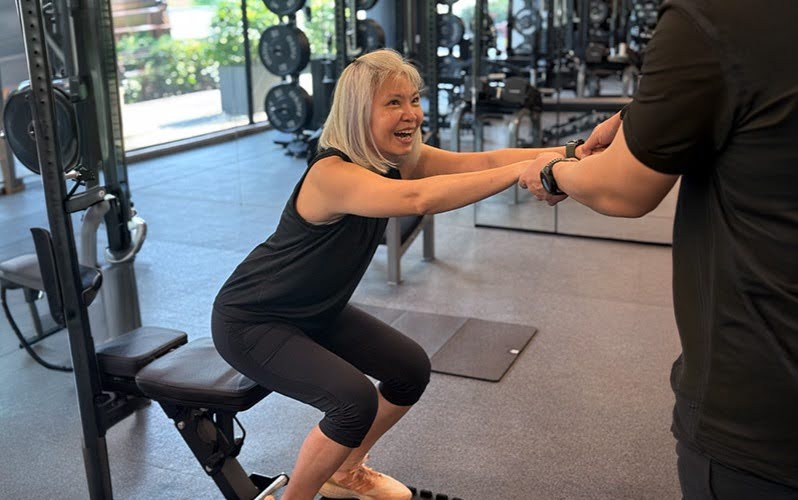 Trainer assisting a senior woman performing squats for improved mobility